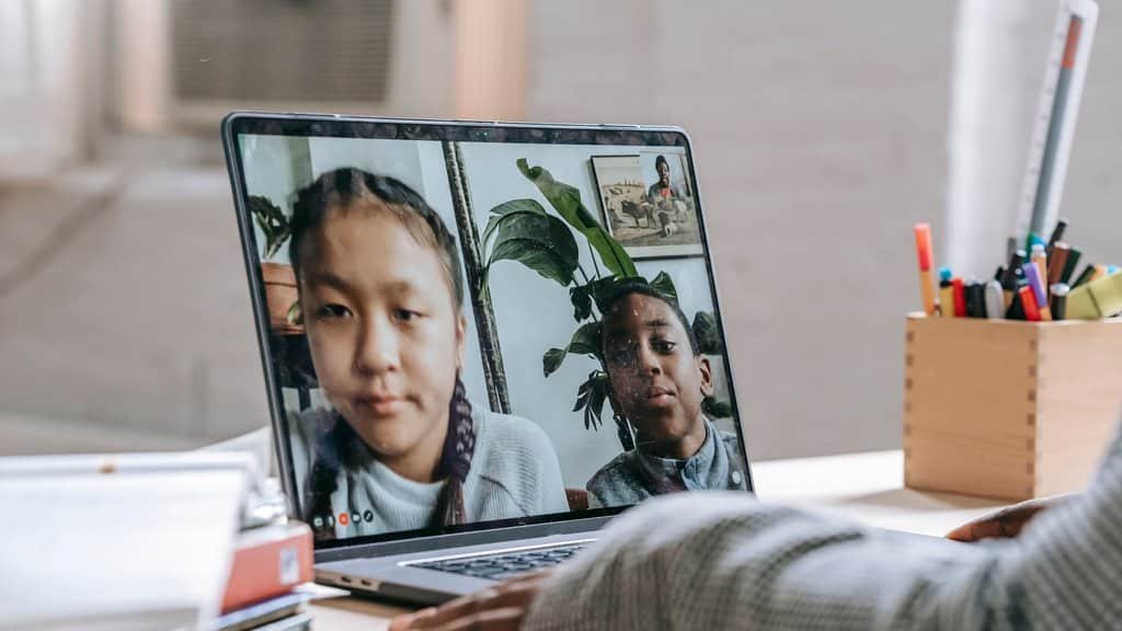 Two students on a live video call with a language teacher, illustrating real-time correction an app cannot give